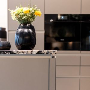 Offener Wohn Essbereich mit Küche Arbeitsplatte Granit Glasfronten Taupe Grau Schwarz Vasen Blumen Backofen