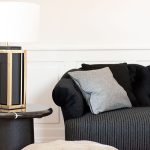Wohnzimmer Einrichtungskonzept schwarzes Sofa graues Kissen schwarz-goldene Tischleuchte