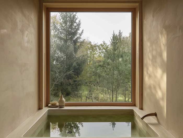 Minimalistisches Badezimmer mit eingelassener Badewanne und großem Holzfenster – natürliche Hausbau Inneneinrichtung mit Fokus auf Ruhe und Ausblick.